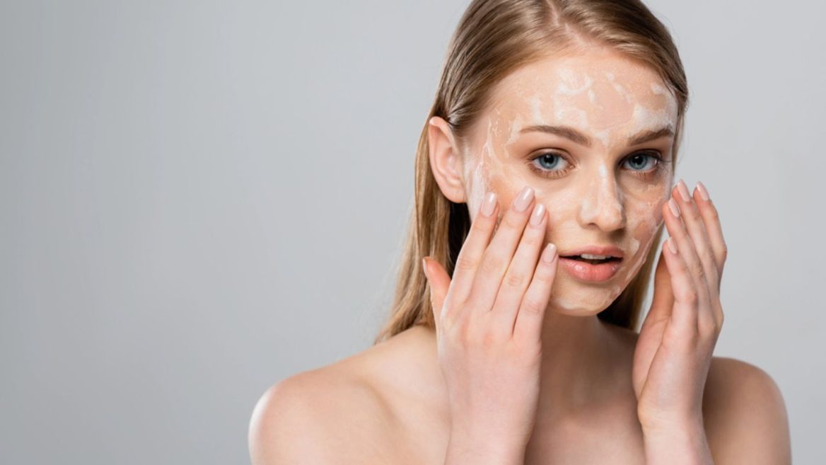 Jeune femme appliquant un peeling léger sur son visage pour améliorer la texture de sa peau, illustrant une routine de soin adaptée aux débutants.